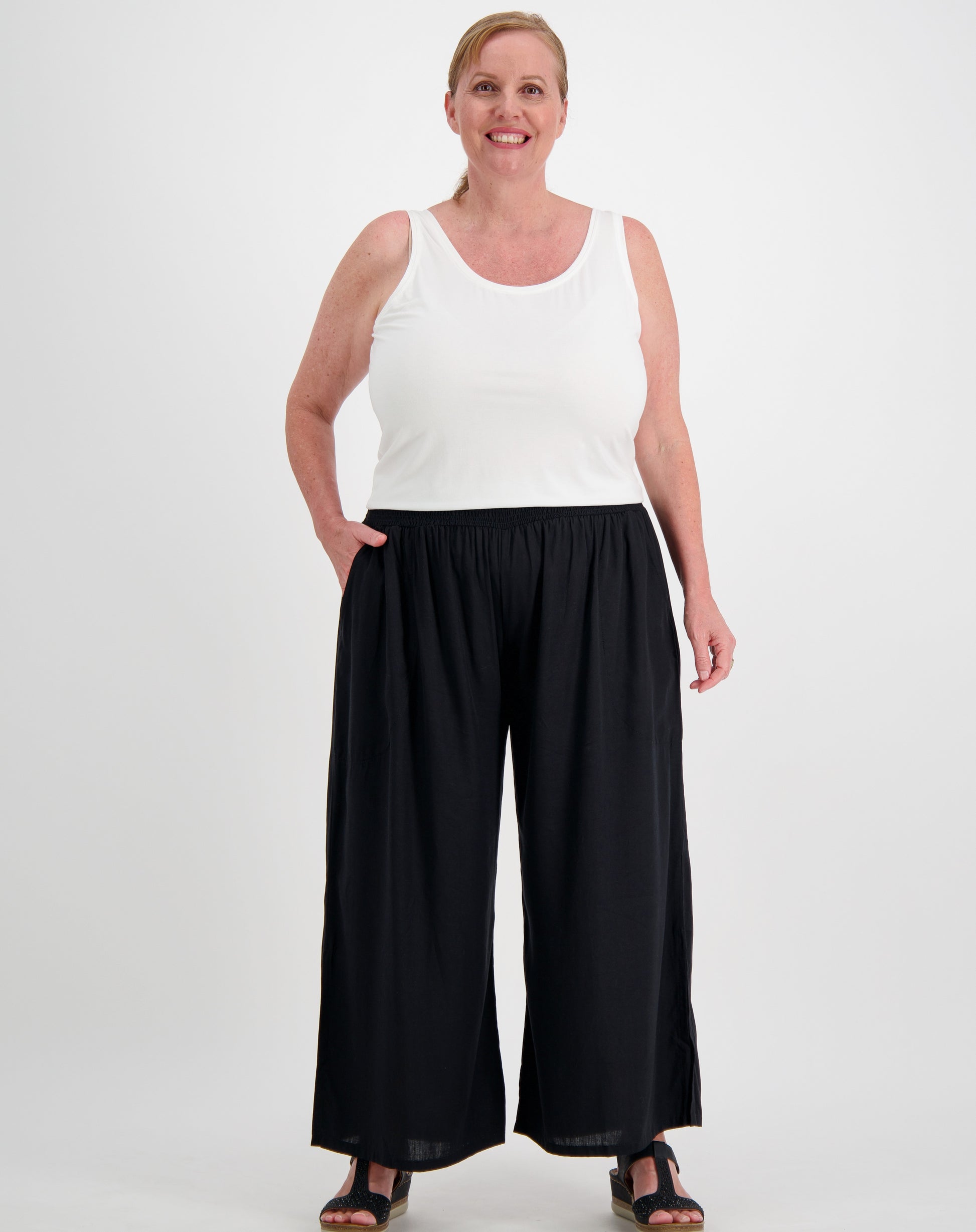 Woman wearing a white sleeveless tank tee in white modal and black wide-leg pants on a white background