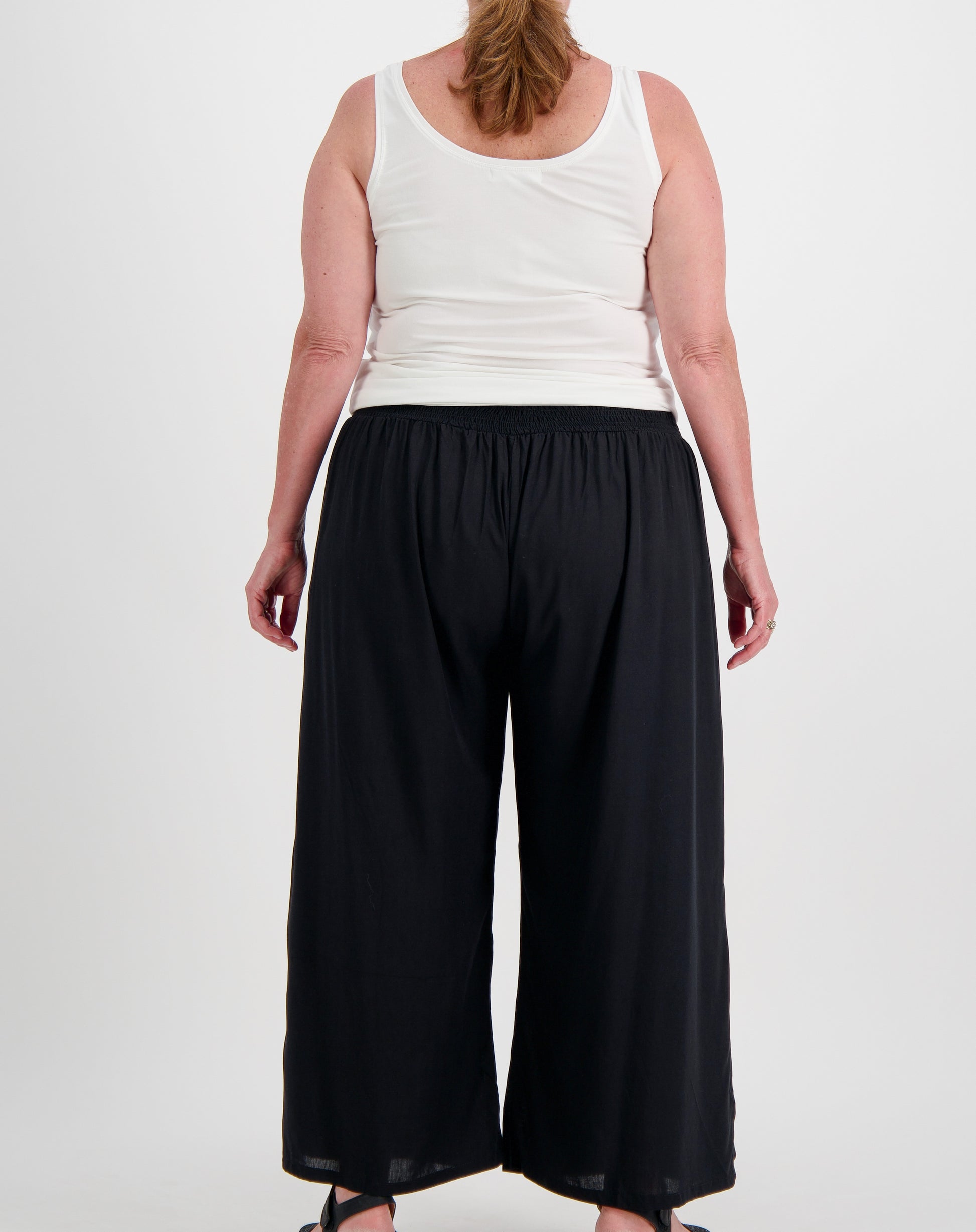 Person wearing a white sleeveless modal top and black wide-leg pants on a white background