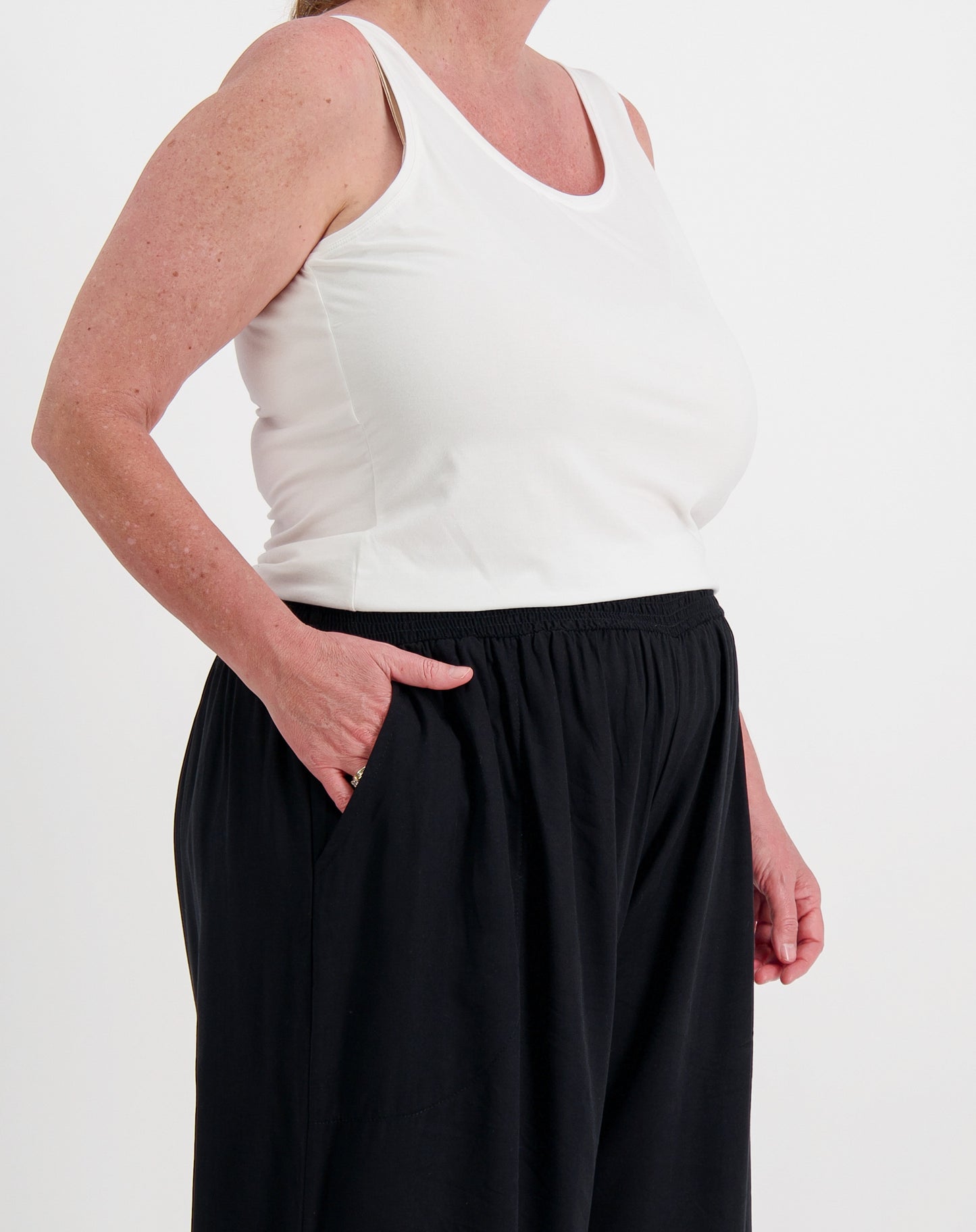 Person wearing a white tank top and black pants with pockets on a white background 