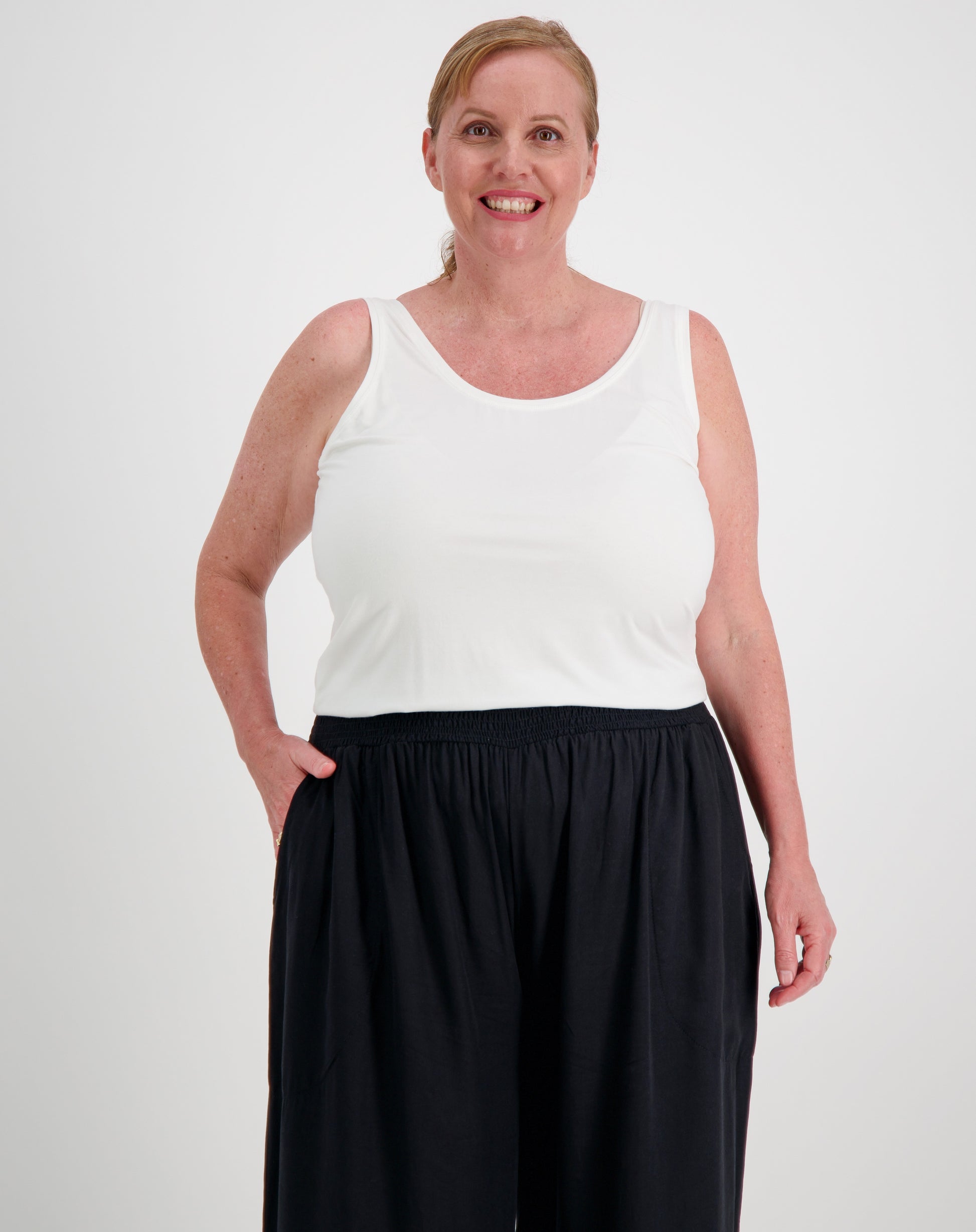 Woman wearing a tank top in white modal  and black pants on a plain background