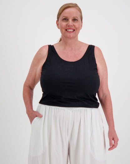 Woman wearing a black tank top in modal by miss seafari and white pants on a white background
