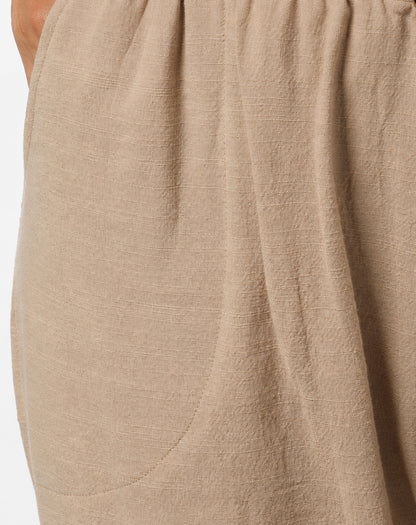Close-up of a natural linen fabric garment with a visible hand holding the edge at the top left, showing the textured weave and drape.