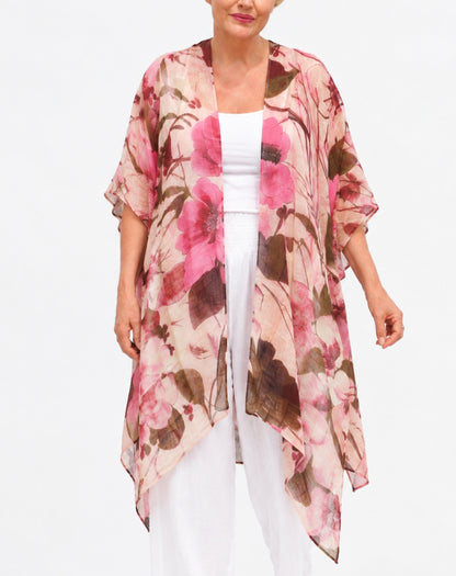 A woman wearing a lightweight floral kimono cardigan with pink, brown, and beige tones over a white top and white pants, photographed against a plain white studio background.