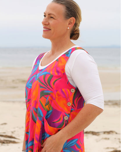 A woman standing on a sandy beach wearing a smock tunic dress with a colorful tropical-print layered with a white short-sleeve scoop tee