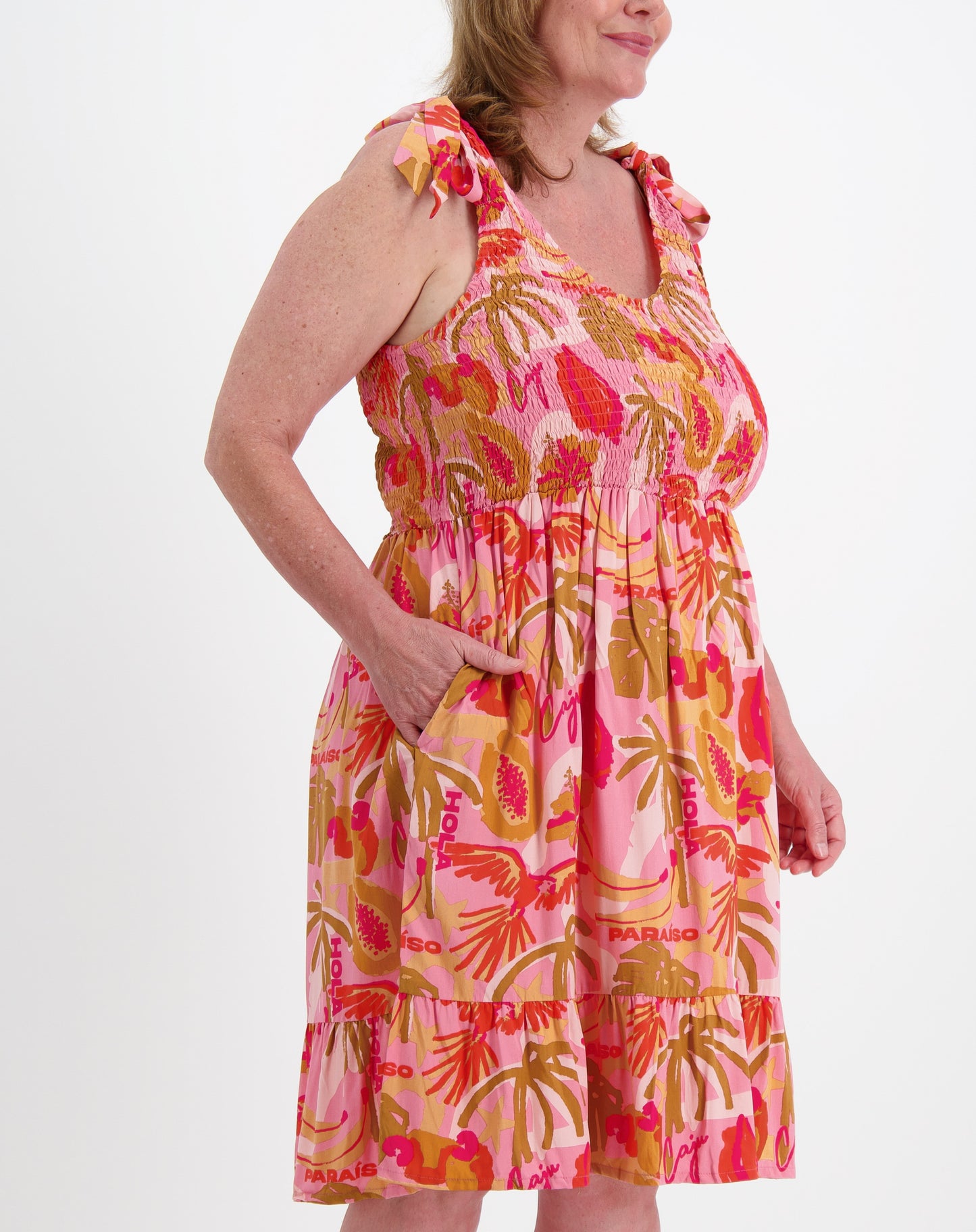 Woman wearing a shirred sundress  in pink paradise tropical print on a white background