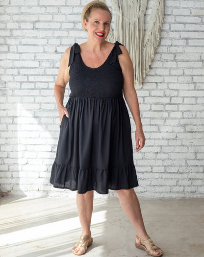 Size 16 Au woman wearing a black shirred dress standing in front of boho villa