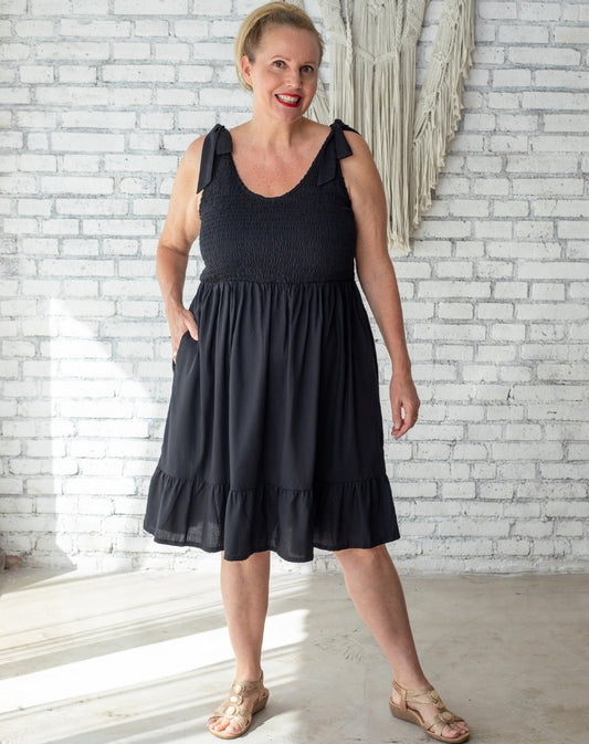 Size 16 Au woman wearing a black shirred dress standing in front of boho villa