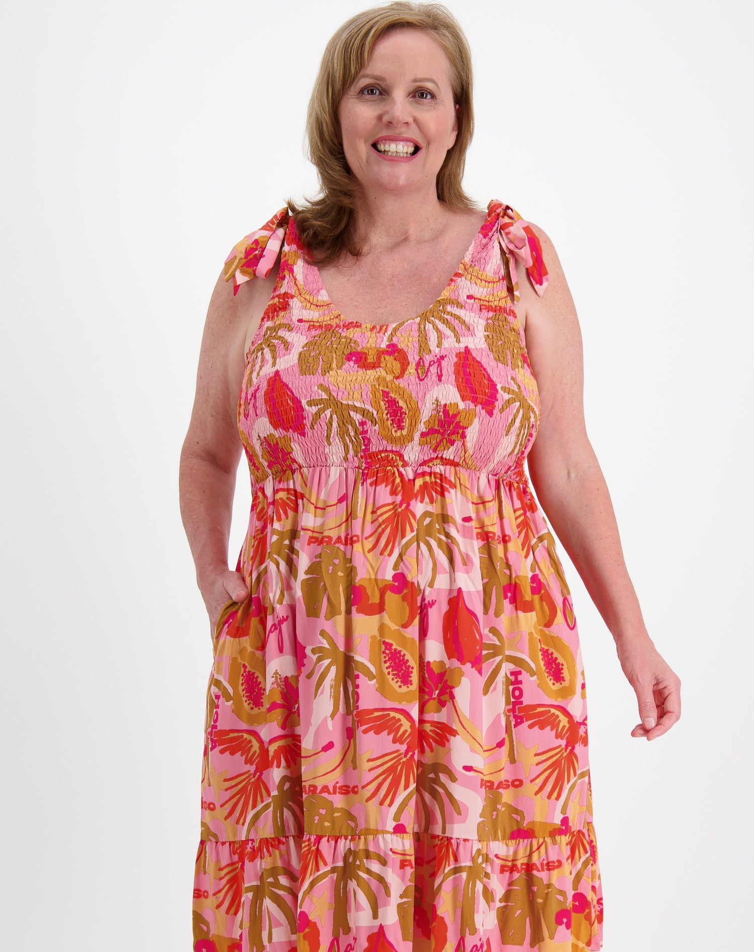 Curve woman wearing a shirred sun dress in pink on a white background