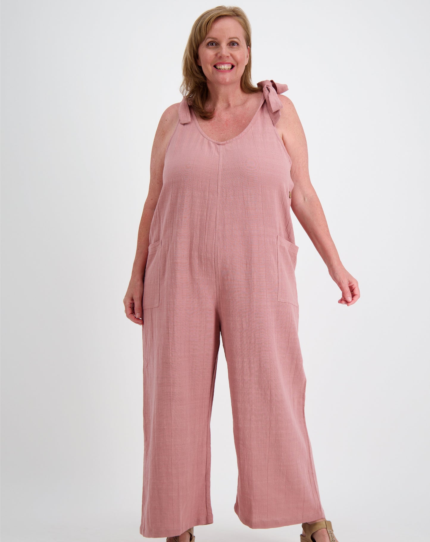 Woman wearing a pink tiestrap jumpsuit by miss seafari on a white background