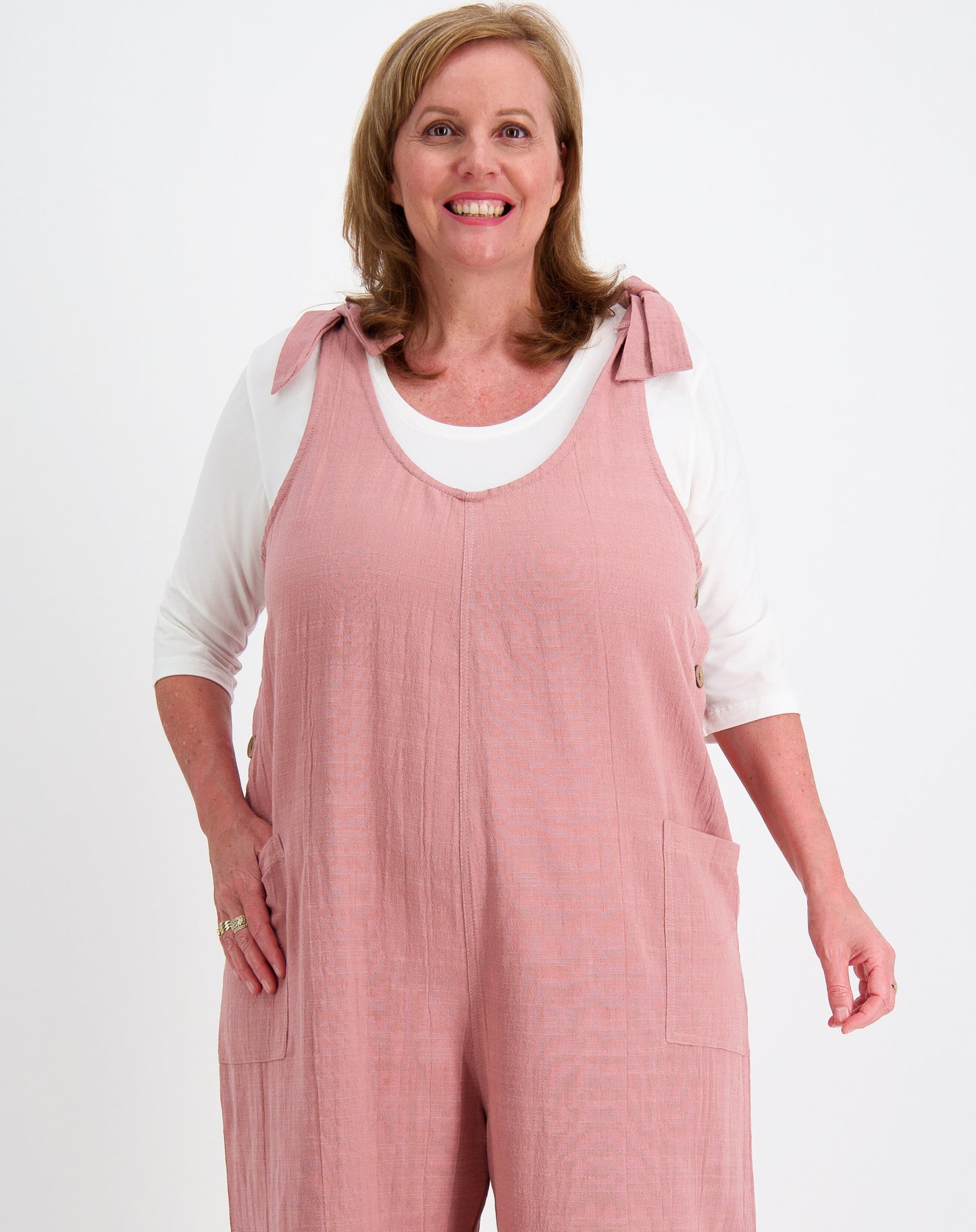 Woman wearing tiestrap jumpsuit in blush with a white modal scoop tee underneath on a white background