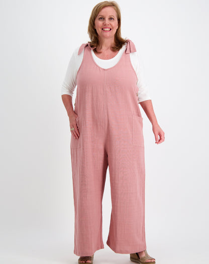 Woman wearing a pink cotton tiestrap jumpsuit with a white modal scoop tee  underneath on a white background
