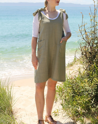 Woman in a green sage smock dress standing on a beach with ocean and moreton island in the background