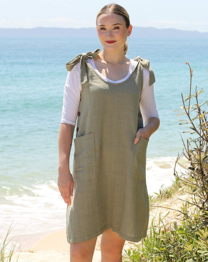 Woman wearing a sage green smock dress with a white tee on a beach