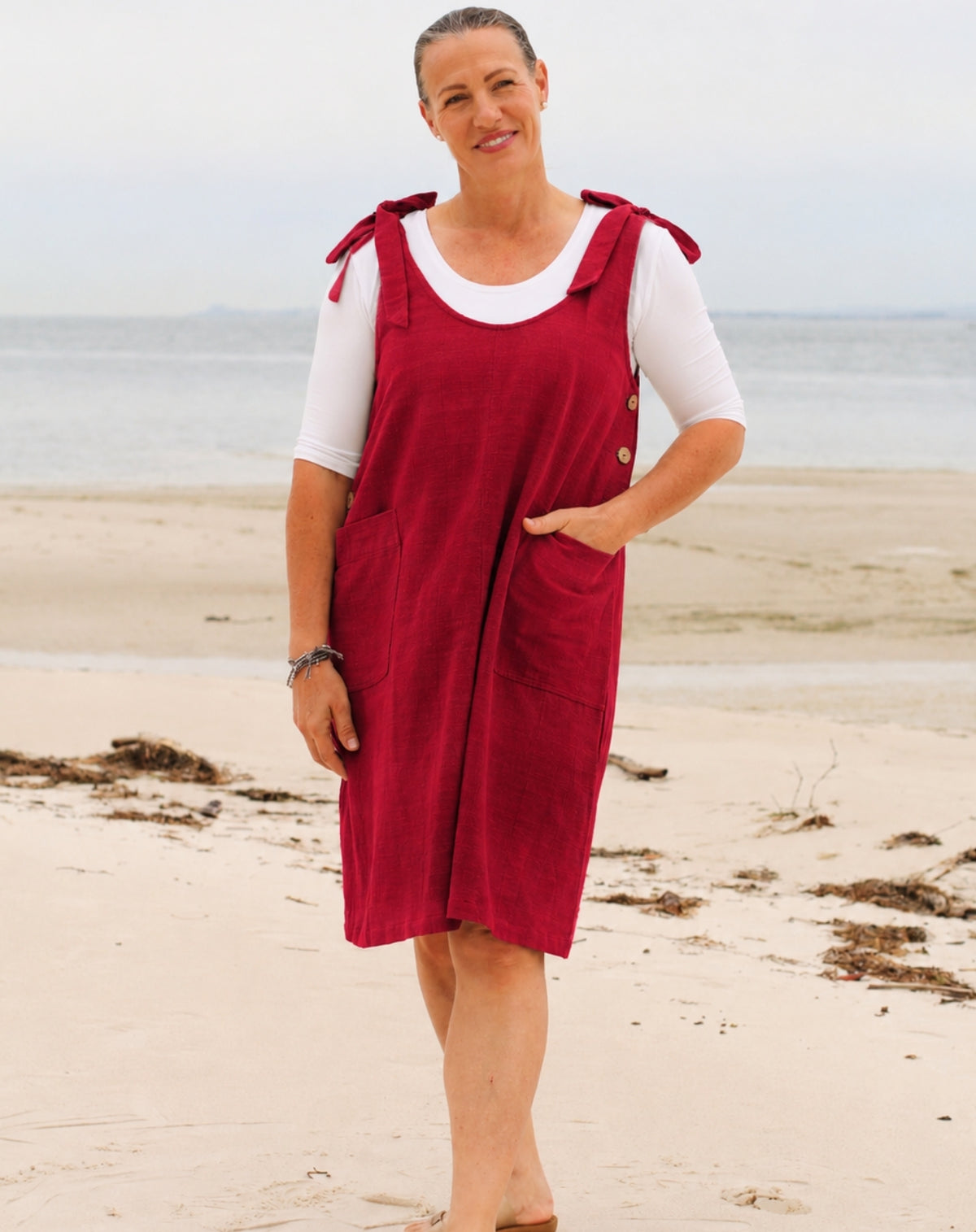 A woman standing on a sandy beach wearing a ruby red smock dress with white short-sleeve scoop tee