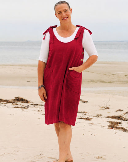 A woman standing on a sandy beach wearing a ruby red smock dress with white short-sleeve scoop tee