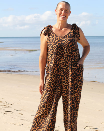 Woman wearing a leopard print jumpsuit with adjustable tie straps on a beach