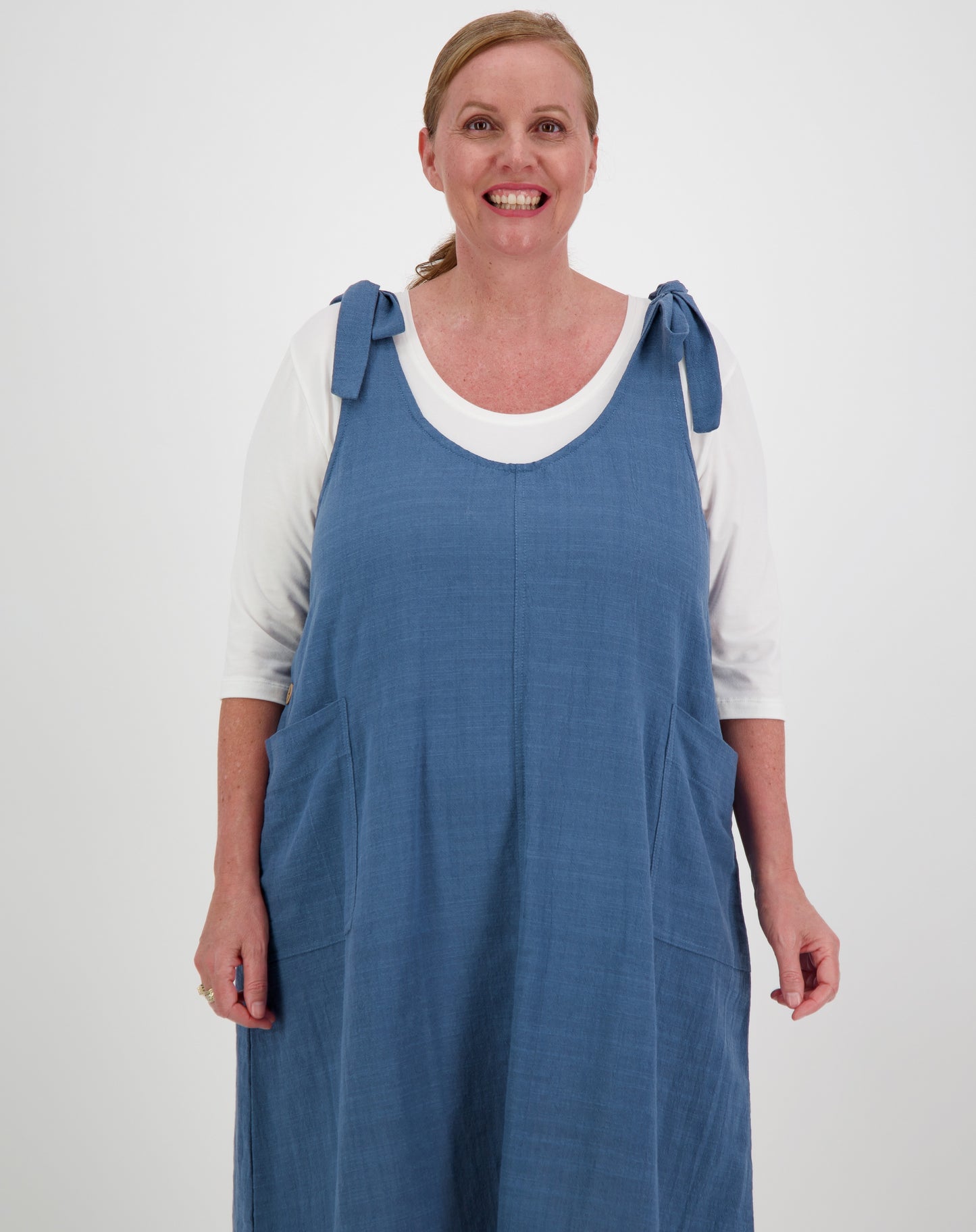 Woman wearing a blue smock pinafore dress over a white shirt on a white background