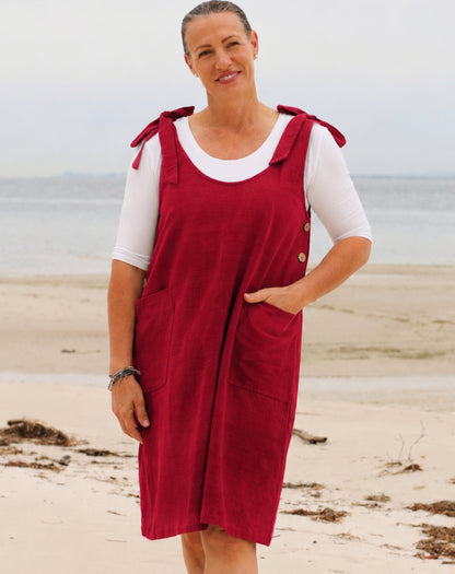 A woman standing on a sandy beach wearing a festive red smock tunic dress over a white short sleeve tee