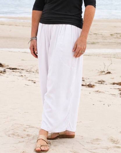 White wide-leg pants worn by a model standing on a sandy beach with the ocean in the background.