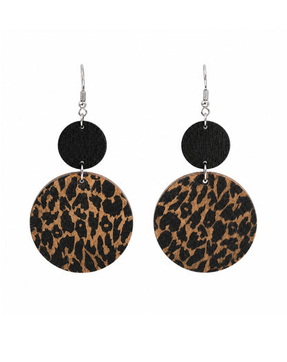 A pair of dangle earrings with silver fishhook wires, a small round black disc, and a larger circular disc featuring a brown and black leopard print pattern, shown against a plain white background.